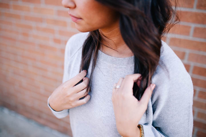 A beautiful woman stands, looking downward, in front of a red brick wall.