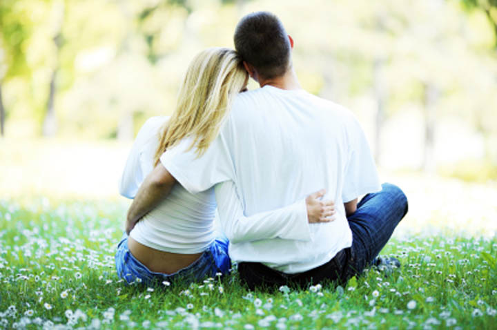 Loving couple sitting and hugging in the park. View from behind.