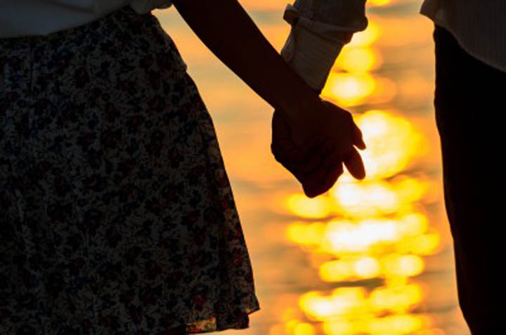Close up of man and woman holding hands in the sunset.