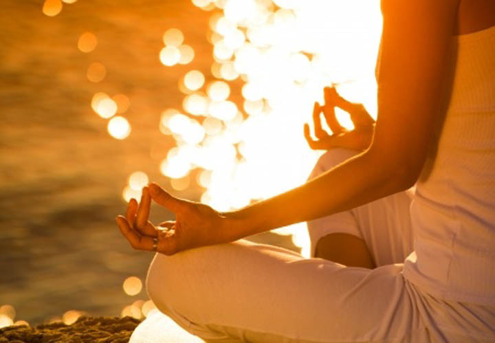 Woman sitting by lake meditating.