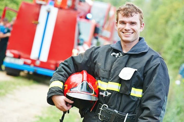 Young smiling fireman firefighter in uniform in front of fire engine machine