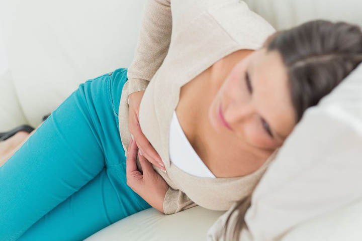 A beautiful woman lies on the couch holding her stomach because she is feeling sick over her breakup.