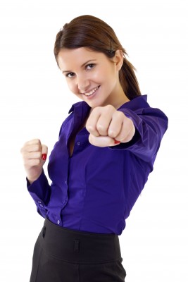 A beautiful brunette woman in a blue blouse and black skirt is punching her fist in the air, showing that she is strong and confident and is ready for commitment.