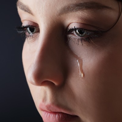 A close-up of the face of a beautiful woman with a tear rolling down her cheek. It's not your fault.