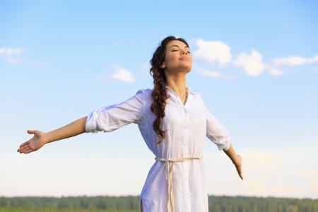 A beautiful woman is standing in a field with her arms outstretched, looking towards the sky as she starts to dream big. 