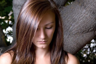 A closeup of a beautiful brunette woman who is looking sad and downward wondering how to get over a break up
