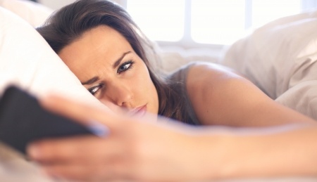 A beautiful brunette woman is laying on her couch looking at her phone upset with a text from a guy that just wants a platonic relationship