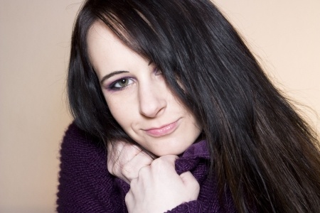 A beautiful brunette woman is pulling her purple sweater close around her neck, looking into the camera and thinking we're all human.