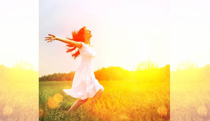A beautiful woman runs through a sunlit field with her arms outstretched, believing in love