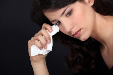 A beautiful woman is holding a tissue to her eyes crying as she is wondering if she should have stuck around instead of breaking up with him.