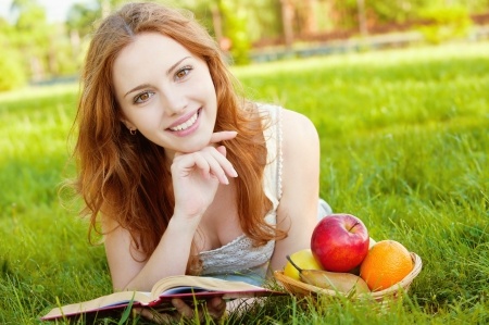 A beautiful woman is lying in the grass reading a book practicing self-love knowing that self love improved her dating life and relationships