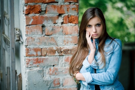 A beautiful woman leans against a wall wondering why she is putting walls up with a great guy in a healthy relationship due to her emotional baggage.