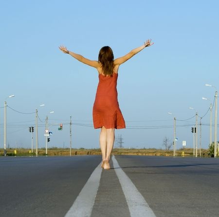 A beautiful brunette woman is walking down the road with her arms extended in joy, happy from the true joy she has found after walking away from a bad relationship.