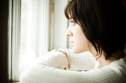 A beautiful woman looks out a window, wondering if she should wait for a commitment or move on from her boyfriend.