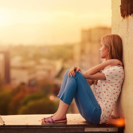 A beautiful woman sits on a balcony overlooking the city devastated that her relationship with her boyfriend has become a long distance relationship