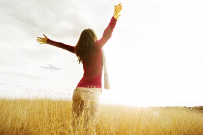 A beautiful woman is rejoicing as she runs through a field in the sunlight.