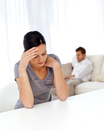 A beautiful woman sits at a table wondering if she should move out while her boyfriend watches tv