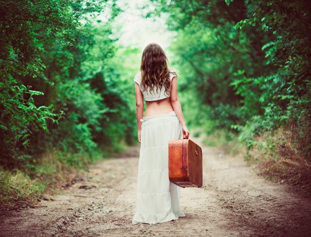 A beautiful woman walks down a path with her suitcase symbolizing that she is breaking free from an emotionally unavailable man who won't commit