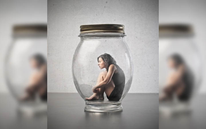 A beautiful woman sits inside of a giant glass jar symbolizing that she feels trapped by her need for external validation.