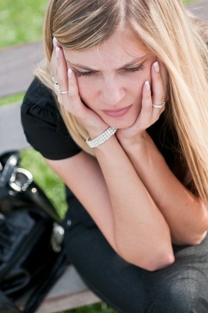 A beautiful woman sits on a park bench with her head in her hands, knowing that she should run from her relationship and not look back, but she still loves him.