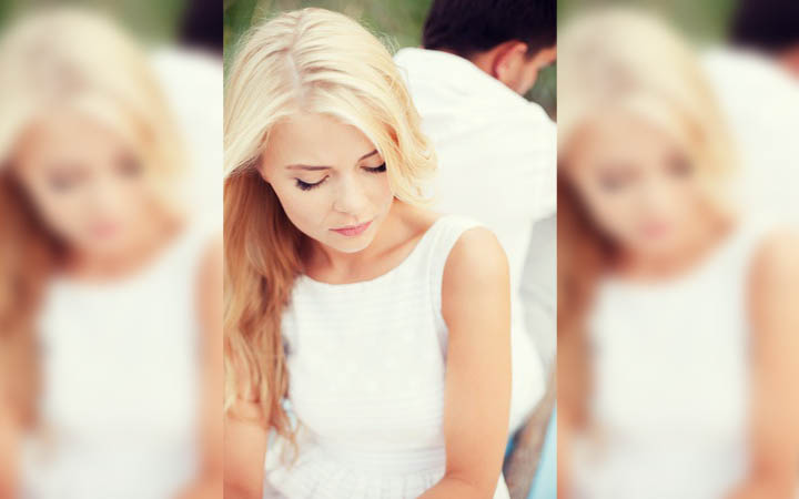 A beautiful blond woman is sitting with her back to her boyfriend as they break up.