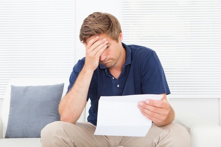 A man is sitting on his couch reading a break up letter, wondering how he is going to survive this break up.