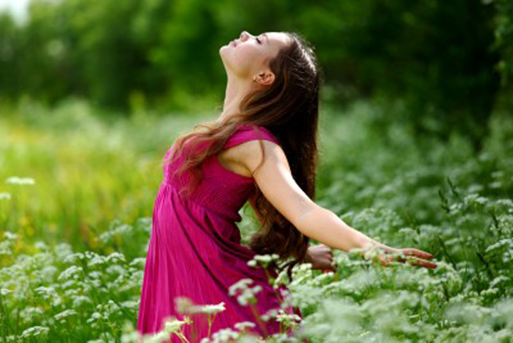 A beautiful woman in a field is looking up, enjoying the sun on her face, recognizing her energy and power.