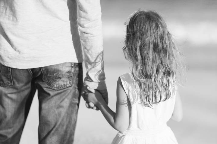 A little girl holds her father's hand while at the beach.