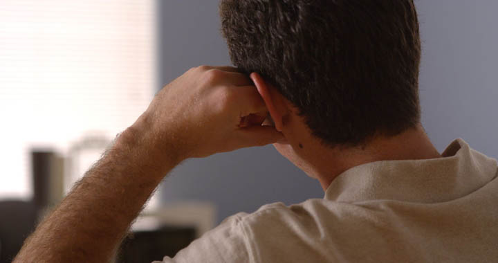 A man sits leaning his head on his arm looking away, afraid of commitment.