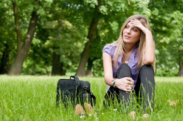 A beautiful woman sitting in a field feeling desperate about her boyfriend.