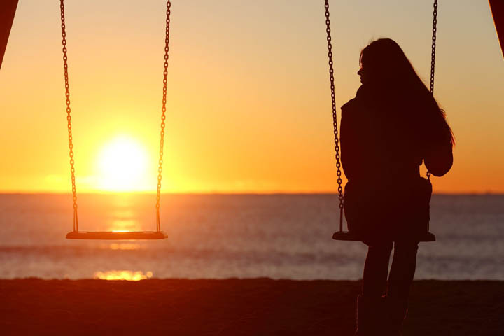 A beautiful woman sits on a swing looking at the ocean, wondering why he's playing with her heart.