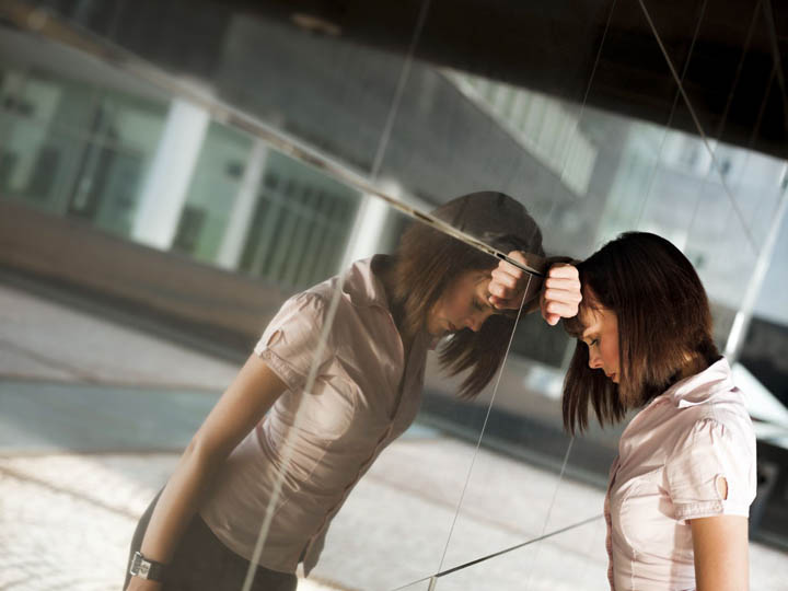 A beautiful woman is leaning her head against a wall, frustrated that her emotionally unavailable ex boyfriend is now in a committed relationship with another woman.