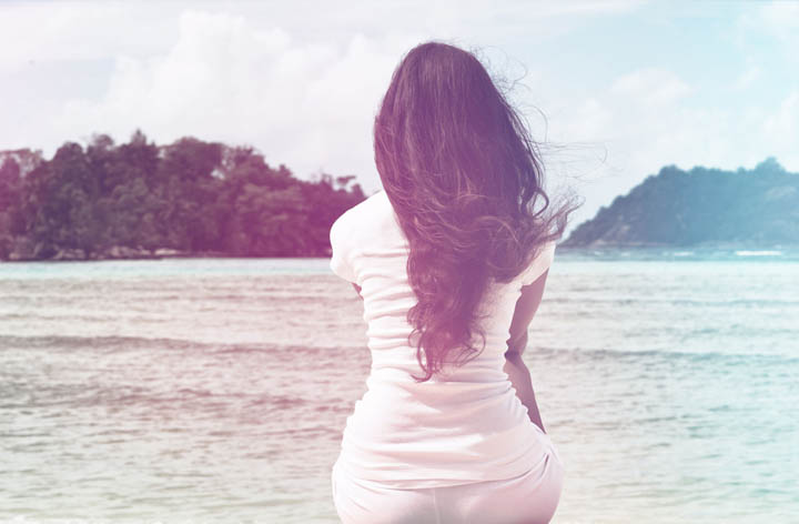 A brunette woman feeling lonely in her relationship sits looking at the ocean.