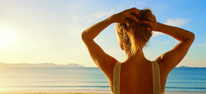 A beautiful woman holds her hair up while looking at the ocean.