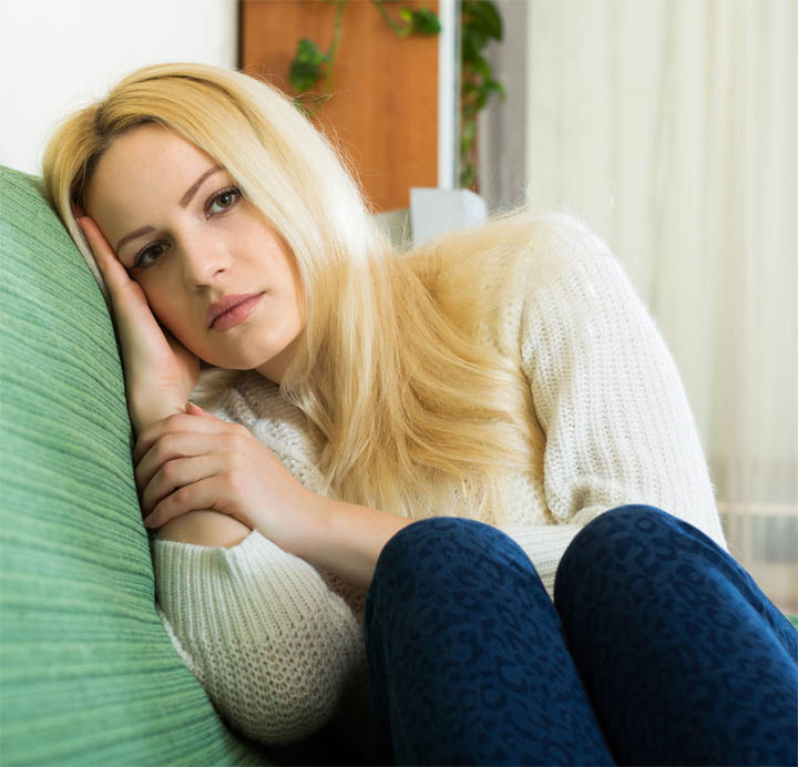 A beautiful woman sits on a couch at home alone, feeling sad that she doesn't have a boyfriend.