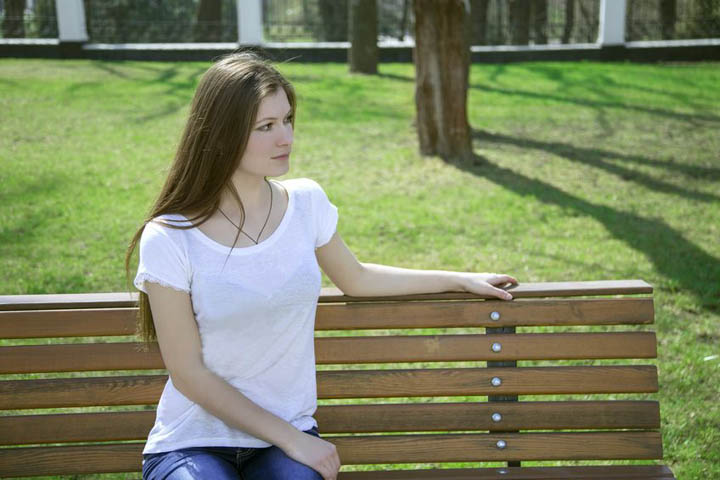 A beautiful woman sits on a bench in a park by herself.