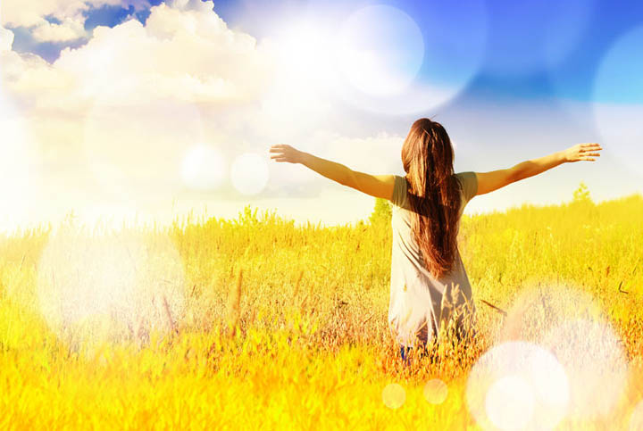 A beautiful, exuberant woman is in a field with her arms raised towards the sun.