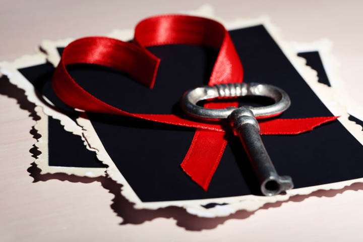 A key lies on a table next to a red heart made from a ribbon.