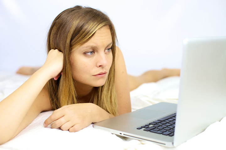 A beautiful woman lies on her bed looking at her laptop.