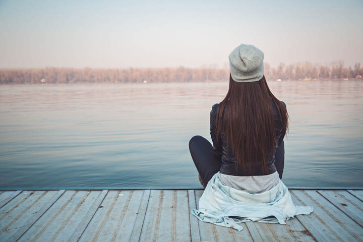 A woman sits on a pier looking at the lake - autumn scene. 