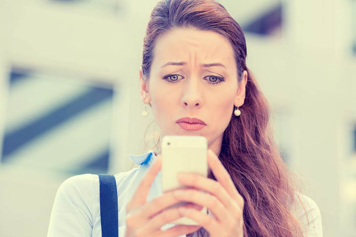 A beautiful woman looks at her phone, worried, wondering if she should call or text him.