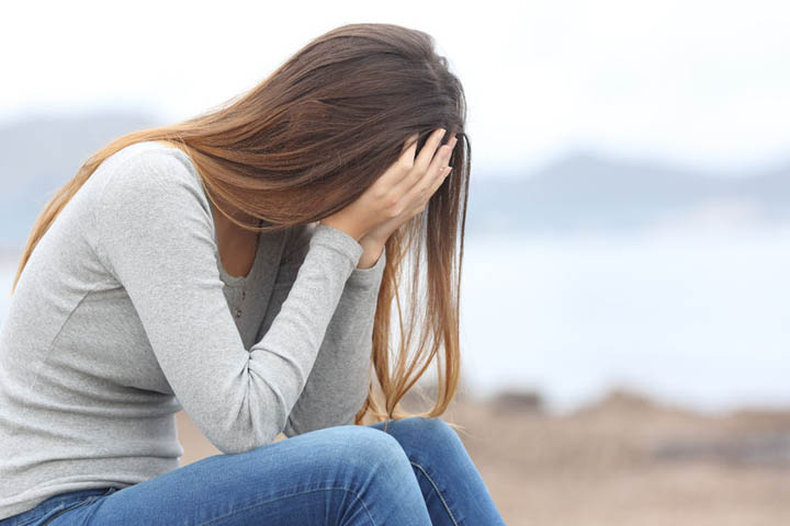 A beautiful woman sits on the beach with her head in her hands wondering if a committed relationship is possible.