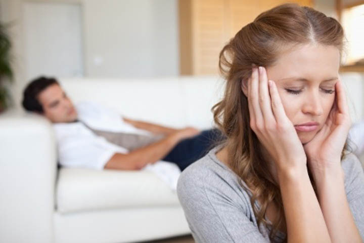 Man lies on the couch while his girlfriend is upset with him because he's emotionally unavailable.