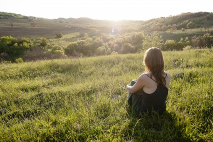 Woman sitting and relaxing in a field, looking at the sun.