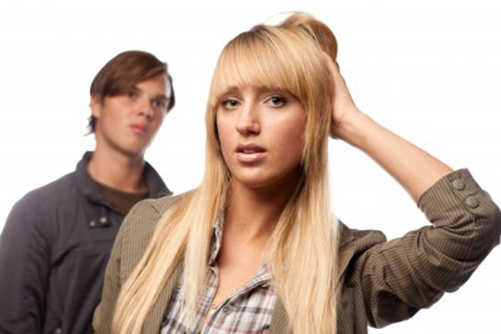 A blond woman scratches her head because she's confused by her boyfriends actions.