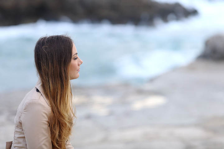 A beautiful woman sits on a beach looking sad because her ex has moved on.