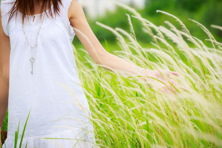 A woman in a white cotton dress is walking through tall grass.