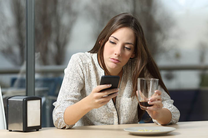 Angry woman stood up on a date in a coffee shop looking at her phone