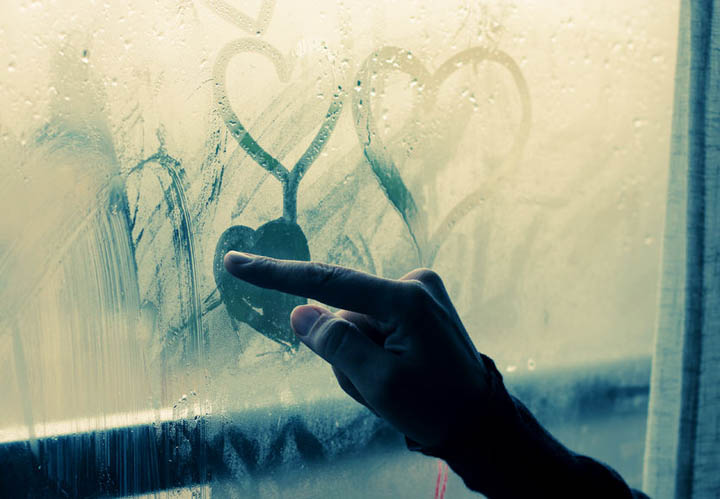 Beautiful 35 year old woman stands in front of the window making hearts on the glass with her finger.