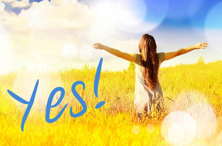 A beautiful woman rising up from the grassy field with her hands in the air proclaiming Yes!